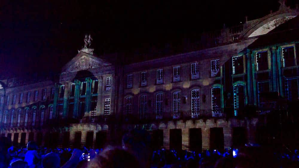 Gebäude bei Nacht mit aufprojizierten Lichtern und dunkler Menschenmenge davor